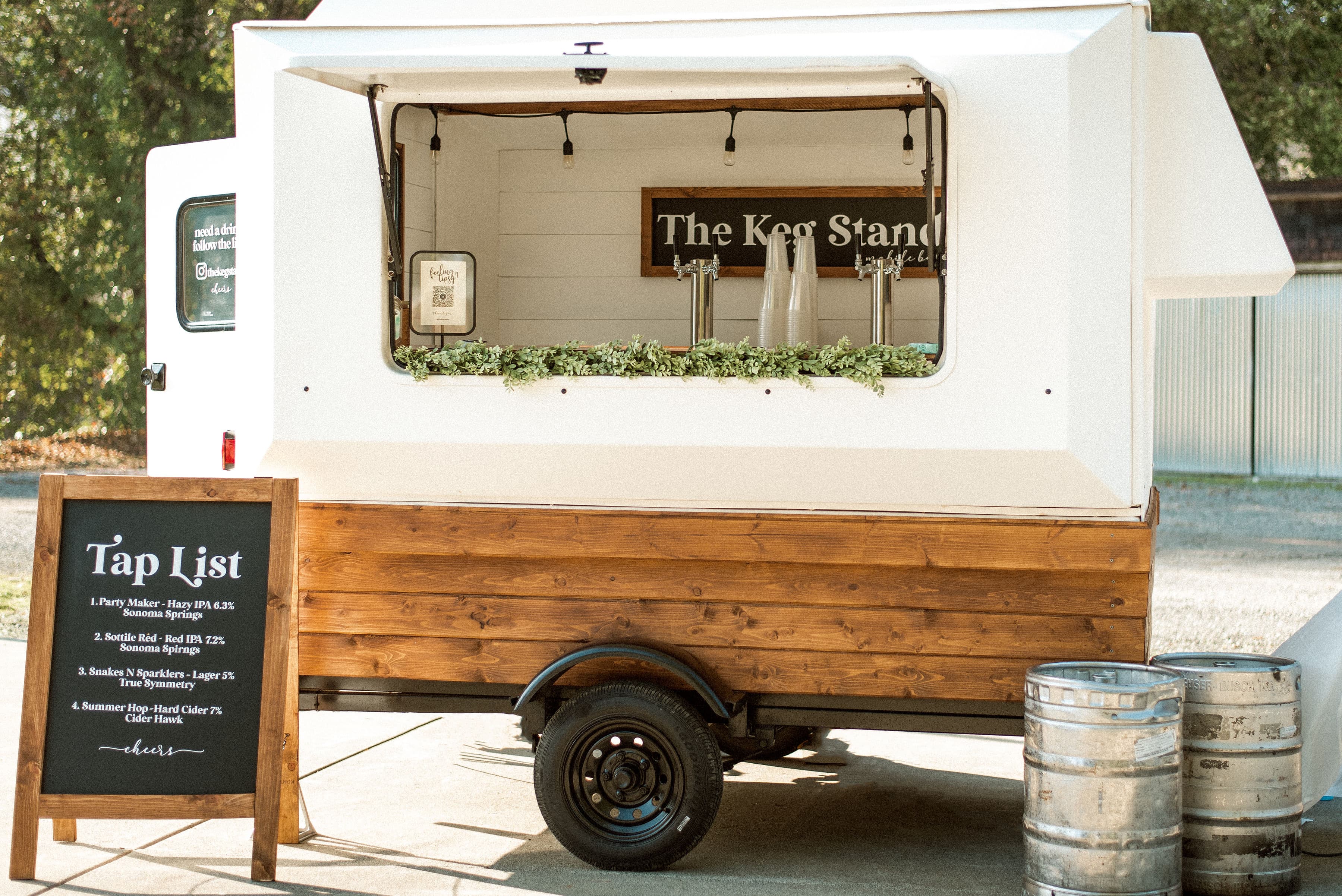 The Keg Stand mobile bar trailer parked at an event, with the tap list chalkboard out front